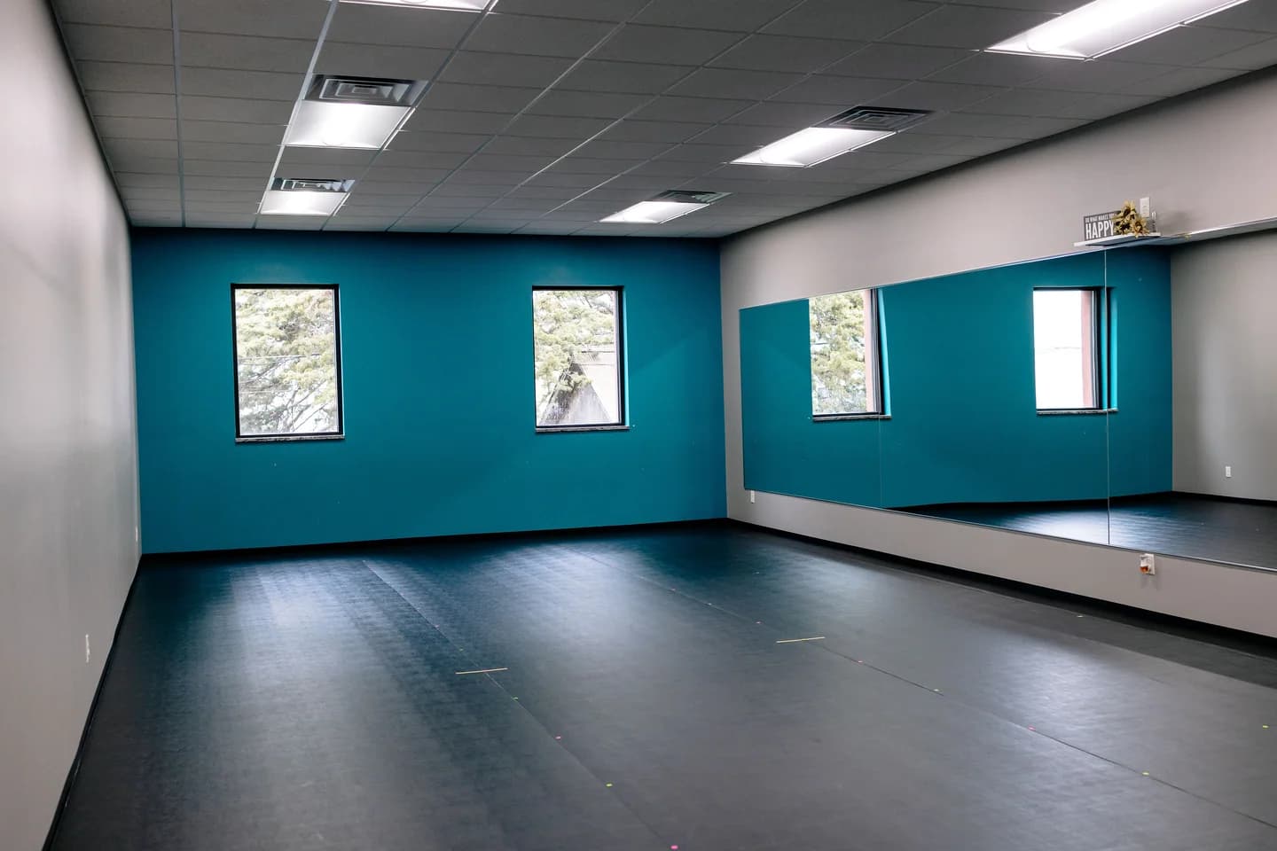 Melinda's Dance Studio Acro Room with black floor, teal-blue wall, and mirrors