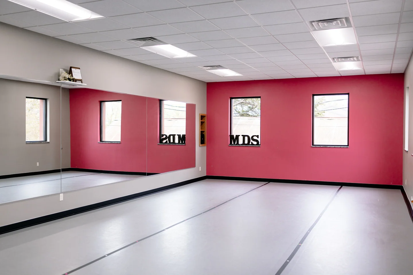 Melinda's Dance Studio Back Studio with dark pink wall, mirrors, and gray dance floor